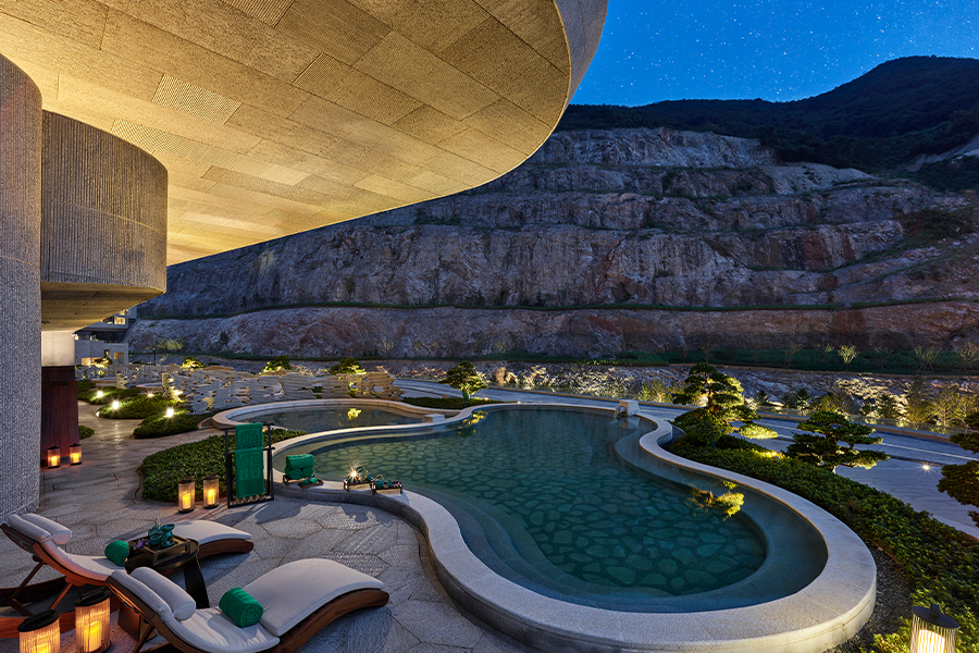 Illuminated pool with loungers amidst rocky landscape at Banyan Tree Nanjing at night.